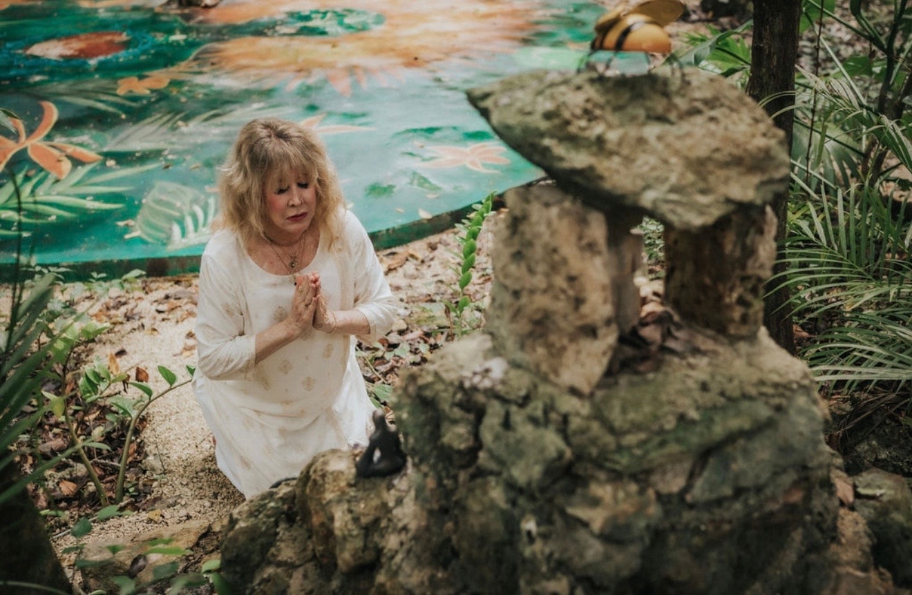 Maureen in prayer at a garden altar in white